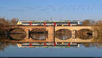 Der mit den Köpfen von Martin Luther und Thomas Müntzer versehene 9442 603 (Bombardier Talent 2) spiegelt sich auf der Saalebrücke bei Halle-Wörmlitz.