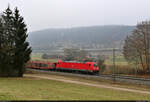 185 253-2 taucht hinter den Bäumen mit Autotransportwagen auf.