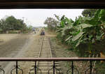 Blick von der offenen Plattform des Salonwagens am Schluss des Tren Crucero auf Bananenplantagen, Motorrad- und Fahrradfahrer sowie Fussgänger zwischen Yaguachi und Naranjito.