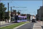 . Reims, Rue Docteur Albert Schweizer - Die violette Bahn 103 biegt hier vom Boulevard de Belges in die Rue Docteur Albert Schweizer. Hier fhrt die Straenbahn auf der Fahrbahn, nur an den Enden ist jeweils ein kleines Stck auf der rechten Seite auf Rasenbahnkrper  um nicht im Autorckstau vor den Kreuzungen warten zu mssen. 23.07.2012 (Matthias)