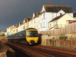 Regionalzug nach Exeter fährt in der Morgensonne vor einer schönen Häuserzeile bei Dawlish nordwärts.