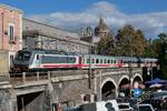 E 464.371 schiebt die Wagen des IC 724, Siracusa - Roma Termini, über eine Steinbogenbrücke in Catania, an und unter der am 17.11.2022 ein Fischmarkt stattfindet