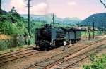 Serie 9600 in Zentral-Kyûshû: Von Kumamoto an der Westküste von Kyûshû aus führt diese Linie hinauf in die Caldera des Vulkans Aso (im Hintergrund sichtbar), und von da an die Ostküste. Die Züge müssen grosse Steilrampen zum Vulkan hinauf überwinden, auch mittels Switchback (Zickzack). Hier ist die 6-9699 mit ihrem Güterzugbegleitwagen gerade rückwärts von der oberen Spitzkehre her in die Station Tateno heruntergekommen. Von hier geht es wieder vorwärts Richtung Kumamoto. 15.August 1972.