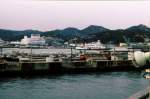 Serie 111 u.113 - auf der Verbindung zwischen Japans Hauptinsel und Shikoku: Bevor die riesige Seto-Brücke (insgesamt 13,1 km lang) 1988 fertiggestellt war, musste in Uno auf die Shikoku-Fähre für die 1-stündige Ueberfahrt umgestiegen werden. Personenzüge durften aus Sicherheitsgründen nicht auf die Fähre. Im Bild der Blick von der Fähre auf den Bahnhof Uno und den Zubringerzug zur Fähre mit Steuerwagen KUHA 111-335. 30.Dezember 1978.