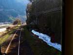 Auf der Strecke der Wakasa-Bahn: im Schatten liegt etwas Schnee, dahinter erheben sich prachvolle alte Familiengrber.