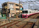 Die Shin Keisei Bahn: Bahnübergang mit ausfahrendem Zug 8803. Tagsüber sieht man wie hier fast nur Mütter mit Kindern; dahinter das schmucklose Gebäude einer Hautklinik. Motoyama, 28.April 2022 