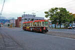 Strassenbahn Hakodate, im Süden der Insel Hokkaidô in Japan, Wagenserie 711-724: Wagen 718 fährt am Denkmal vorbei, welches an die Ankunft riesiger Zahlen von Geflüchteten