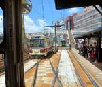 Nagasaki Strassenbahn – aus Gebrauchtmaterial zusammengebaute Wagen, Serie 1200. 1982 gebaute Wagen Nr. 1201-1205, 2x38 kW Motoren, nur die Wagenkasten sind neu, alles andere ist gebrauchtes Material. 1202-1205 erhielten 2003-5 modernere elektrische Steuerungen (statt Handkurbel) und Motoren (2x45 kW) von eingestellten Strassenbahnen im Nordosten der Insel Kyûshû. Im Bild fährt Wagen 1205 aus der Haltestelle  Hauptbahnhof  aus, während der grüne Wagen 1201 von hinten einfährt. 8.August 2013. 