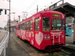 Takaoka Manyô-Linie, alte Wagen Serie 7070: von diesen 1967 beschafften Wagen sind noch 5 Stück im Einsatz. Im Bild steht Wagen 7076 am Bahnhof von Takaoka, 28.Februar 2010. Er trägt noch den alten Werbeanstrich, in welchem der örtliche Götterschrein Takase Jinja für seine Dienstleistungen wirbt, nämlich Rituale des Lebenslaufs, Hochzeitsfeiern, das Arrangieren von Pärchenbeziehungen und das grosse Fest des Neujahrstags. Kein Zufall, dass der Wagen mit Herzchen geschmückt ist! 