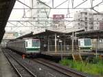 Tokyo Metro Chiyoda-Linie, Serie 6000: Zwei Züge in Abiko, links Zug Nr. 24 (westseitiger Endwagen 6124), rechts Nr. 27. 11.Juli 2010. Der Schaffner von Zug Nr.24 betätigt gerade die Bahnsteigmelodie, die anzeigt, dass die Türen gleich geschlossen werden. 