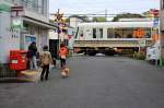 Japanische Stadtquartiere - ein JR-Zug der Serie 221 am Bahnübergang von Ôbaku an der Linie zwischen Kyoto und Nara. 7.April 2015. 