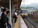Serie 221: Am nassen und stickigen Morgen des 18.Juni 2011 wollen sich viele Menschen in den Zug drängen, um von Rokujizô nach Kyoto zur Arbeit zu fahren. Einfahrt des Zuges mit Steuerwagen KUHA 221-3. 
