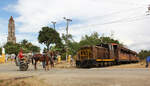 Typische Szenerie auf dem Land in Iznaga: der Touristenzug 'Valle de los Ingenios' (Tal der Zuckermühlen) mit einer kleinen Diesellok wartet auf die Abfahrt nach Trinidad, währenddem sich das Landleben mit Mensch und Tier auf der Hauptstras ...