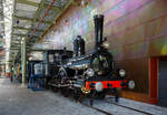 Die Dampflokomotive HSM 89  Nestor , sp�ter NS № 1010 (NS-Baureihe 1000) am 29 April 2025 im Het Spoorwegmuseum (bis 2005 NSM - Nederlands Spoorwegmuseum / Niederl�ndischen Eisenbahnmuseum) in Utrecht im ehemaligen Bahnhof Maliebaan.

Die Dampflok wurde 1879 von Borsig in Berlijn-Tegel unter der Fabriknummer 3730 gebaut und an die damalige HSM - Hollandsche IJzeren Spoorweg-Maatschappij (Holl�ndische Eisenbahn-Gesellschaft) geliefert, 1880 erfolgte die Inbetriebnahme.

HSM 89  Nestor  ist eine niederl�ndische 1B (2-4-0) Tenderlokomotive, die vom Niederl�ndischen Nationalbahnmuseum erhalten wurde. 29 seiner Art wurden f�r den NS-Vorg�nger Hollandsche IJzeren Spoorwegmaatschappij (HSM) gebaut.

In den fr�hen Tagen war die HSM die einzige Eisenbahngesellschaft in den Niederlanden, die ihren Lokomotiven immer einen Namen sowie eine Nummer gab. Der Nestor zum Beispiel wurde auch die Zahl 89 zugewiesen. Trotz der Tatsache, dass es immer als  Der Nestor  bezeichnet wurde, zeigt das Namensschild nur  Nestor . Diese Serie von Lokomotiven wurde  Tenners  genannt, weil sie mit Dampfdruck in H�he von 10 Atmosph�ren umgehen konnten. Ein bemerkenswertes Merkmal dieser Lokomotivserie ist, dass der F�hrerstand der aus Holz und nicht aus Metall besteht. Ihre Lokf�hrer und Heizer wurden daher manchmal  Woonwagenbewoners  genannt, was ungef�hr  Caravan-Bewohner  bedeutet. Metallstangen, die als Schienenw�chter bekannt sind, wurden an der Vorderseite der Rahmenplatten befestigt. Der Lokf�hrer konnte Besen zu diesen Wachen montieren, um die Schienen unter verschneiten Bedingungen zu r�umen. Wie alle Lokomotiven hat der Nestor auch Fettt�pfe montiert. Diese T�pfe w�ren mit Fett und Garn gef�llt oder gef�hlt, um die Achsen zu schmieren.

HSM
Mit dem Ausbau einer Eisenbahnlinie und der Er�ffnung einer weiteren 1879 wurde die Notwendigkeit, ihre Sammlung von Lokomotiven zu erweitern, deutlich und bestellte 29 dieser Maschinen in Borsig. Sie waren 74-82, 89-98 und 116-125 nummeriert, weil die HSM Lokomotiven anhand des Empfangsauftrags nummerierte. Die Serie hie� EOS - JORDAENS, die Namen von 74 und 125. Trotz der Namensschilder, die nur einen Namen haben, wurden sie in der Sprache immer als Der Name bezeichnet (z. B.  Der Nestor  statt  Nestor ).

Bei ihrer Ankunft erhielten verschiedene �ltere Lokomotiven weniger wichtige Arbeiten, die noch �ltere Lokomotiven aus dem Dienst zogen. Mit der Ankunft neuer Sharp Stewart-Lokomotiven im Jahr 1890 wurden die EOS - JORDAENS auf sekund�re, weniger wichtige Aufgaben reduziert, wie sie es zuvor bei �lteren Lokomotiven getan hatten. Sie arbeiteten in den Depots Almelo, Amsterdamer Hauptbahnhof, Apeldoorn, Haarlem und Zutphen und den meisten gro�en Stationen entlang einer Linie nach Osten nach Westen mitten im Land. Sp�ter verteilten sie sich noch mehr auf andere HSM-Depots, die immer mehr auf Rangierarbeiten reduziert wurden.

NS
Bedingt durch den Ersten Weltkrieg wurde 1917 eine Zweckgemeinschaft der unabh�ngigen Eisenbahngesellschaften HSM beziehungsweise HIJSM (Hollandsche IJzeren Spoorweg-Maatschappij) und SS (Maatschappij tot Exploitatie van Staatsspoorwegen) gegr�ndet. Die beiden Gesellschaften errichteten einen gemeinsamen Bahnbetrieb, blieben aber rechtlich unabh�ngig. Dies �nderte sich 1938, als HIJSM und SS vollst�ndig fusionierten und in der AG NS (Nederlandse Spoorwegen, fr�her Nederlandsche Spoorwegen geschrieben) aufgingen. Das Rollmaterial wurde bereits 1921 zusammengelegt, so wurden die EOS - JORDAENS zu NS 1001 - 1029 nummeriert. Die NS vergr��erte auch die Fenster in der Kabine.

Bis 1923 befanden sich acht von ihnen am Hauptbahnhof Utrecht, der vor der Fusion ausschlie�lich Staatsspoorwegen-Gebiet war. Sie wurden ausschlie�lich zum Rangieren verwendet. In Amersfoort waren f�nf weitere mit der gleichen Arbeit und in Winterswijk, vier, obwohl diese vier auch Z�ge zu einigen nahe gelegenen Bahnh�fen fuhren. 1924 wurde jedoch die Mehrheit der NS-1000 in die westlichsten Depots, einschlie�lich Apeldoorn, verlegt.

Elf der Baureihe wurden 1921-1923 ausgemustert. Der NESTOR �berlebte mit dem Rest bis 1934. In diesem Jahr schickte NS alle bis auf zwei, NS 1010 & 1011, auf den Schrottplatz. Ein Jahr sp�ter folgte auch NS 1011. Obwohl der NESTOR (NS 1010) auch 1934 abgeschafft werden sollte, half die NVBS (Niederl�ndische Vereinigung der Interessenten in der Eisenbahn- und Stra�enbahnindustrie) dabei, sie f�r das noch zu bauende niederl�ndische Eisenbahnmuseum zu erhalten, so dass sie in Boxtel gelagert wurde.

Die Lokomotive wurde zusammen mit anderen f�r das Museum reservierten Rollmaterial ein paar Mal w�hrend des Zweiten Weltkriegs bewegt. 1944 war die NESTOR in Maastricht, dort wurde sie den zur�ckweichenden Deutschen schwer besch�digt (gesprengt). Als der Krieg endete, wurde die Maschine eine Weile in Almelo gelagert, immer noch schwer besch�digt. Erst 1953 erteilte die NS die Erlaubnis, sie zu reparieren. Die Reparatur wurde 1964 abgeschlossen. In diesem Jahr fuhr die Lokomotive die letzten 100 Meter alleine zum niederl�ndischen Eisenbahnmuseum, obwohl die n�tige Energie mit Druckluft aus einem Diesel geliefert wurde.

Der NESTOR war die letzte NS-Lokomotive, die f�r Museen restauriert wurde. Sie bekam ihren Look aus den 1880er Jahren, einschlie�lich der Holzkabine mit hohen Fenstern.

Im niederl�ndischen Eisenbahnmuseum ist NESTOR nicht der einzige Ex-NS 1010. Die Baunummer der Baureihe 1000 wurde sp�ter f�r Elektrolokomotiven verwendet, deren Zehnter ebenfalls erhalten blieb.

TECHNISCHE DATEN:
Typ: Schnelldampflok
HSM-Serie: EOS - JORDAENS, ab 1921 NS 1001 - 1029
Spurweite: 1.435 mm (Normalspur)
Achsfolge: 1B (engl. 2-4-0)
L�nge �ber Puffer: 14.160 mm (Lok 8.260 mm + Tender 5.900 mm)
Treibraddurchmesser: 1.860 mm (neu)
H�chstgeschwindigkeit: 90 km/h
Gesamtheizfl�che: 93,5 m�
max. Dampfdruck: 10,3 kg/cm�
Anzahl der Zylinder: 2 (� 406 mm x 558 mm Hub)
Eigengewicht: Lok 38,8 und Tender 25,1 t = 63,9 t
Anh�ngelast: 3560 kg
Wasservorrat: 9 m�
Kohlevorrat: 3,6 t