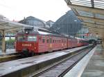69 003 in alten Farbdesigne, zweiteilig, und 69 081 in modernen Farbdesigne, dreiteilig am 21.06.2006 im Bahnhof Bergen abfahrbereit als Nahverkehrszug nach Voss.