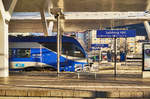 Blick auf die Bahnhofsschilder von Salzburg Hbf, während gerade ein Meridian nach München abfährt.