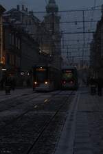 In düsterer Abendstimmung am 5.1.2026 kreuzen in der verschneiten Grazer Altstadt die beiden Variobahnen Nr. 232 und 211.
Im Hintergrund ist die Stadtpfarrkirche zum Heiligen Blut zu sehen.