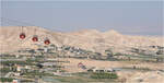 Die fast tiefste Seilbahn der Welt -     Drei Gondeln der Jericho-Seilbahn vor einem kargen Höhenzug im Jordantal.