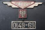 Polen Parowozownia Wolsztyn Strecke 328 Leszno-Wolsztyn-Zbąszynek: Ol49-69 (Fablok, Fabryka Lokomotyw, Chrzanów, Fabriknummer 3180, 1953), Schmuck der Rauchkammertür, Leszno, 8. April 2022. Zur weiteren Frontzier der Ol49-69 gehört auch ein diskretes Hufeisen. Die Aufnahme entstand bei Gelegenheit einer Mitfahrt im Zug 77627 Leszno-Wolsztyn durch die (nicht ganz saubere) Fensterscheibe des Wagenüberganges. Die Ol49-69 ist seit Oktober 2021 die einzige betriebsfähige Dampflok in Wolsztyn. Während ihrer periodischen Wartung alle dreissig Tage können die Zugpaare 77236/77505 und 77228/77627 Wolsztyn-Leszno-Wolsztyn jeweilen mehrere Tage nicht dampflokbespannt verkehren. Vgl. die Internetseiten parowozy.com.pl und parowozowniawolsztyn.pl.