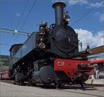 Die portugiesische Dampflok CP E164 von La Traction präsentiert sich in Glovelier nach dem Wasserfassen in voller Schönheit, während ihre Füsse noch auf der Strasse stehen,