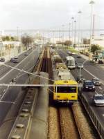LISBOA (Distrikt Lisboa), 24.01.2001, rechts ein Vorortzug der Linha Cascais der Ausfahrt in den Bahnhof Belém, links ein Zug bei der Ausfahrt (Bahn-Linksverkehr in Portugal); im Hintergrund die imposante Ponte 25 de Abril -- Foto eingescannt