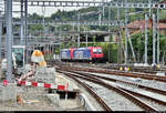 Im Grenzbahnhof Chiasso (CH) sind Re 484 018-7 SBB und eine unbekannte Schwesterlok der SBB Cargo AG hinter Baumaterial abgestellt.