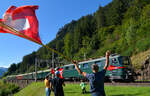 Gotthard-Bahntage: Auf der Talfahrt von Göschenen nach Erstfeld kommt Ae 6/6 11411 pfeifend an Xaver Andermatt und seinem Fahnenspalier vorbei. 18.09.2021