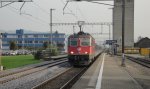 Vollstrom mit gehobenem Frontpanto durchrast die Re 4/4  11215 mit dem RE Luzern-Olten die Haltestelle Brittnau-Wikon.