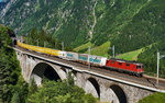 Die Re 4/4 II 11277 (420 277-6) fährt am helllichten Tag mit einem Postzug über die mittlere Meienreussbrücke talwärts.