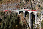 Bernina-Express mit den Panoramawagen von Chur nach Tirano auf dem Landwasserviadukt in der Nachmittagssonne, fotografiert vom Fotopunkt 'Süd'. Dieser ist ab dem Bahnhof Filisur in etwa 20 Minuten zu Fuss sehr gut erreichbar. Filisur, 16.10.2025