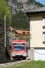 Der Regionalzug -der Matterhorn-Gotthard-Bahn fährt zwischen Mauer und Haus aus dem Bahnhof Göschenen nach Andermatt. Göschenen, 11.5.2024