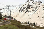 Die Lokomotive HGe4/4 102 der Matterhorn-Gotthardbahn bringt den Glacier Express vom Oberalppass her nach Nätschen herunter. Sehr auffällig ist die gelb-braune Farbe des Schnees, die von Sahara-Sand her stammt. 6.Mai 2024 