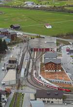 Blick auf den Bahnhof Andermatt aus dem Richtung Oberalppass fahrenden Zug am 06.05.2024: Am Bahnsteig ein Deh 4/4 I und rechts ein Deh 4/4 II