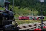 Während die HG 3/4 4 der DFB am 5. Juli 2015 in Oberwald auf die Abfahrt über die Furka Bergstrecke nach Realp wartet, kommt der von MGB HGe 4/4 II 3  Dom  angeführte Glacier Express auf seinem Weg von St. Moritz nach Zermatt gerade aus dem 673m langen Umgehungstunnel gefahren. Kurz zuvor hat er den Furka-Basistunnel von Realp her durchfahren.