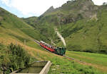 Brienz Rothorn Bahn: Abstieg der Dampflok 12 (Baujahr 1992) mit ihren Wagen 9 und 3. Im Vordergrund wohl eine Kuhtränke; die Lok trinkt ihr Wasser in der Mittelstation Planalp. 3.August 2023 