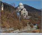 Vor der mächtigen, ab 1922 erweiterten und im Jahre 1958 eingeweihten Wahlfahrtskirche  Madfonna del  Sangue  in Re fährt etwas versteckt, ein SSIF  Treno Panoramico  Vigezzo Vision als D 47 P Richtung Camedo.
19. März 2015