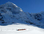 Kleiner Zug vor grossem Panorama: Triebzug der Jungfraubahn fährt mitten im Schnee von der KLeinen Scheidegg nach Eigergletscher. Links der Berg 'Mönch', rechts oben auf dem Grat befindet sich die (unterirdische) Station Jungfraujoch (3454 müM). Kleine Scheidegg, 11.1.2024