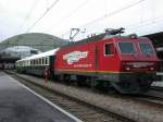 Voralpenexpresslok 015 der SOB (ex Re 4/4 IV der SBB) mit einem Sonderzug in Chur bestehend aus einem Speisewagen und einem Velowagen der Bodensee Toggenburg Bahn. (26.03.2004) Im Hintergrund ist die Halle der Postautostation zu sehen.