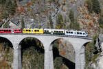 Farbenprächtiger gehts nicht! Ahnenzug (Farbgebung Chur - Arosa, RhB, Bernina-Bahn) als IR38 von Chur nach St. Moritz auf dem Landwasserviadukt in der Nachmittagssonne, fotografiert vom Fotopunkt 'Süd'. Dieser ist ab dem Bahnhof Filisur in etwa 20 Minuten zu Fuss sehr gut erreichbar. Filisur, 16.10.2025