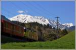 Oben in den Bergen regiert noch der Winter, unten fährt RE1224 mit Ge 4/4 II 611  Landquart  bereits durch saftig grüne Wiesen, hier zwischen Reichenau-Tamins und Trin. (20.04.2015)