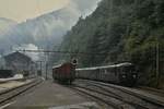 An einem völlig verregneten Julitag 1983 kommt ein RBe 4/4 der SBB auf seiner Fahrt von Moutier nach Delemont im inzwischen stillgelegten Bahnhof Choindez an. Im Hintergrund sind die Hallen des von Roll-Werkes und die damals noch eingesetzte E 2/2 9 sichtbar.