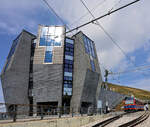 Ferrovia Monte Generoso: Nach mehrj�hrigem Umbau der Gipfelstation Monte Generoso hat der bekannte Architekt Mario Botta f�r seine Heimat ein imposantes Geb�ude namens  Steinblume  (Fiore di Pietra) errichtet, neben dem sich Triebzug 14 der Generoso-Bahn ganz klein ausnimmt. 23.Juli 2026 
