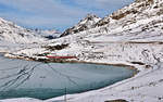 Zum rechten Moment kommt zur Abwechslung ein R nach Tirano,der aus den RhB Triebzügen ABe 8/12 3506 und des 3511 mit einem einzelnen Wagen hintennach gebildet wurde,am Lago Bianco vorbei der an diesem Morgen mit einem gewaltigen Krachen und Aechzen am zufrieren war.(Tags darauf war er komplett zu und schneebedeckt).Bild 24.11.2017