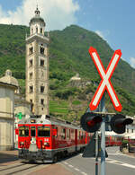 Die Heiligen Kreuze der Berninabahn: Umringt und gesichert, nicht nur, von Andreaskreuzen kommen die ABe 4/4 III 54 und 56 der Rhätischen Bahn (RhB) mit einem  Bernina-Express  am 15. Juni 2022 langsam als  Straßenbahn  über den Piazza Basilica im italienischen Tirano gerollt und erreichen in Kürze den dortigen Bahnhof. Im Hintergrund sind die Basilika Madonna di Tirano und auf dem Felsen am Berg die Chiesa di Santa Perpetua zu erkennen.