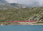 Roter Zug in hochalpiner Landschaft: Regionalzug von St. Moritz nach Tirano hat vor kurzem die Station Ospizio Bernina (2253 müM) verlassen und fährt entlang des Lago Bianco in Richtung Alp Grüm. Ospizio Bernina, 7.8.2025