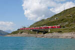 See, Zug und Berge: der Regio von St. Moritz nach Tirano hat vor wenigen Augenblicken die Station Ospizio Bernina (2253 müM) verlassen und fährt dem Lago Bianco entlang in Richtung Alp Grüm. Und nein, der Fotograf steht nicht im Wasser, sondern auf einer kleinen Halbinsel. Ospizio Bernina, 7.8.2025