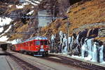 Mit einem PmG haben ABe 4/4 II 46 (SWS/SAAS/BBC 1965) und ein weiterer ABe 4/4 II im März 1996 die Station Alp Grüm erreicht, am Zugende zwei mit Baumstämmen beladene Flachwagen und ein gedeckter Güterwagen. Strenge Nachtfröste und trotz strahlendem Sonnenschein geringe Tagestemperaturen haben das herunterfließende Wasser am Hang gefrieren lassen.