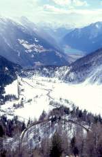 RhB REGIONALZUG 431 von St.Moritz nach Tirano am 09.03.1998 in der Stablini-Kehre mit Triebwagen ABe 4/4III 52 - BD 2473 - AB - B - Uah - Uah - Kk. Hinweis: Blick von der winterlichen Alp Grm (2091m)  ber den 12km entfernten schneefreien Lago di Poschiavo (962m), Seelnge 2,5km bis zu den Bergamasker Alpen. Links ist die schneebedeckte Kreuzungsstation Cavaglia erkennbar.
