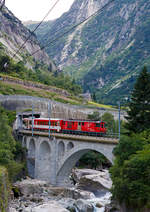 Die MGB Deh 4/4 I – 55 „Brig“ schiebt am 01.08.2019 den Schöllenenbahnzug von Göschenen nach Andermatt nach hinauf und überquert hier gerade die Reuss. 

Die Strecke Göschenen–Andermatt ist die Schöllenenbahn, eine einspurige Zahnradbahn (Zahnstangensystem Abt) im Schweizer Kanton Uri. Sie durchquert die Schöllenenschlucht der Reuss und weist eine Maximalsteigung von 179 Promille auf, die steilste im MGB-Netz. Die Bahnstrecke wurde zwischen 1913 und 1917 durch die Schöllenenbahn AG (SchB) gebaut. Die Schöllenenbahn AG fusionierte 1961 mit der Furka-Oberalp-Bahn (FO), welche wiederum  zum 1. Januar 2003 mit der Zermatt-Bahn (BVZ), zur heutigen Matterhorn-Gotthard-Bahn (MG) fusionierte. 

Heute befördert die Schöllenenbahn im Jahr ca. 400.000 Reisende. Sie hatte in der Vergangenheit auch eine große militärische Bedeutung. Sie versorgte die Festungsanlagen des Réduit im Gotthardmassiv. Die Bahnstrecke hat eine Gesamtlänge von 3.770 Metern, davon sind 2.509 mit Zahnstange ausgerüstet. 1.022 Meter der Strecke befinden sich in Tunneln und 1.110 Meter in Galerien. Die Bahn fährt durch fünf Tunnel und fünf schützende Galerien. Vier Mal fährt die meterspurige Schmalspurbahn über eine Brücke.

Auf der Schöllenenbahn wurden ursprünglich vier zweiachsige Elektrolokomotiven für kombinierten Adhäsions- und Zahnradbetrieb von SLM und BBC mit Bezeichnung SchB HGe 2/2 eingesetzt. Ursprünglich liefen sie mit 1.200 Volt Gleichstrom. 1941 wurden sie auf 11.000 Volt Wechselstrom umgestellt. Die letzte dieser vier Lokomotiven wurde 1985 Später kamen kamen FO BCFhe 2/4 der Schweizerischen Lokomotiv- und Maschinenfabrik mit einem Antrieb der BBC zum Einsatz. ausrangiert. Heute (2019) befahren Deh 4/4 und Wagen der Matterhorn-Gotthard-Bahn die Strecke. Dabei befindet sich das Triebfahrzeug stets am talseitigen Ende, am Zugschluss läuft ein Steuerwagen.

Die Schöllenenbahn bietet einen stündlichen Pendelverkehr an und ist in den Fahrplan der SBB und der Matterhorn-Gotthard-Bahn vollständig integriert.
