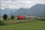 1116 045 legt sich vor den Chiemgauer Bergen mit dem EC 114  WRTHERSEE , auf der Reise von Klagenfurt Hbf nach Dortmund Hbf, in die Kurve.